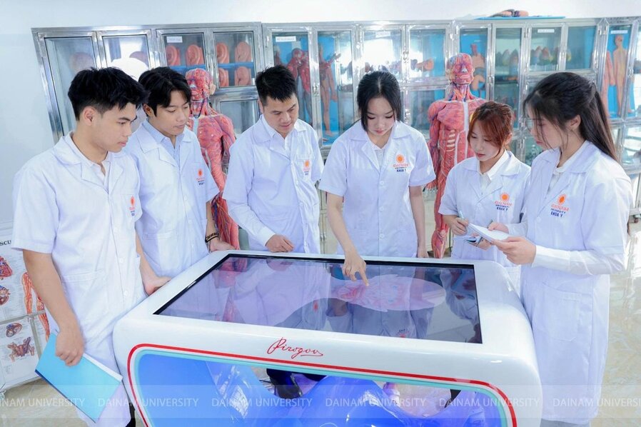 A group of people in white coats standing around a large touch screen

Description automatically generated